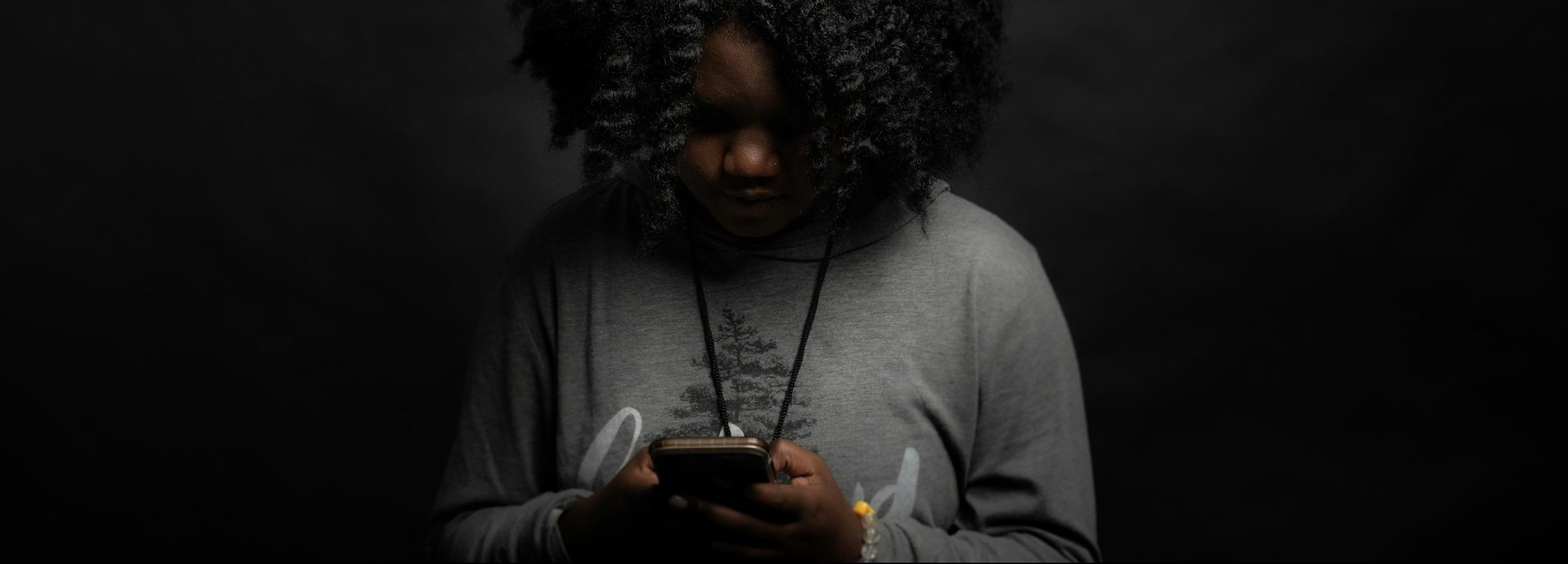 Woman looking down at phone in the dark technology-facilitated gender-based violence