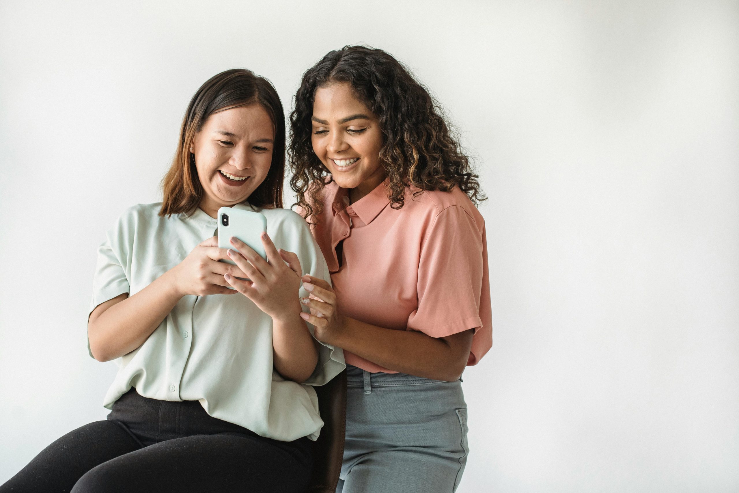 Two women smiling and looking at a phone technology-facilitated gender-based violence