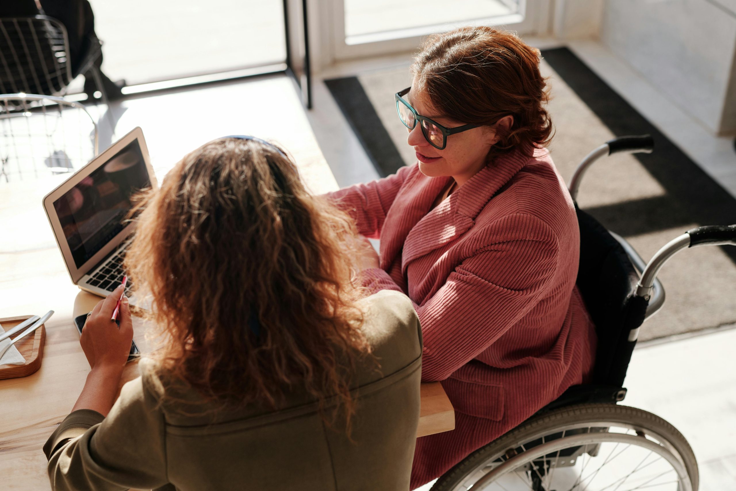Bird’s eye view of woman in wheelchair in front of laptop next to another woman Technology-facilitated gender-based violence