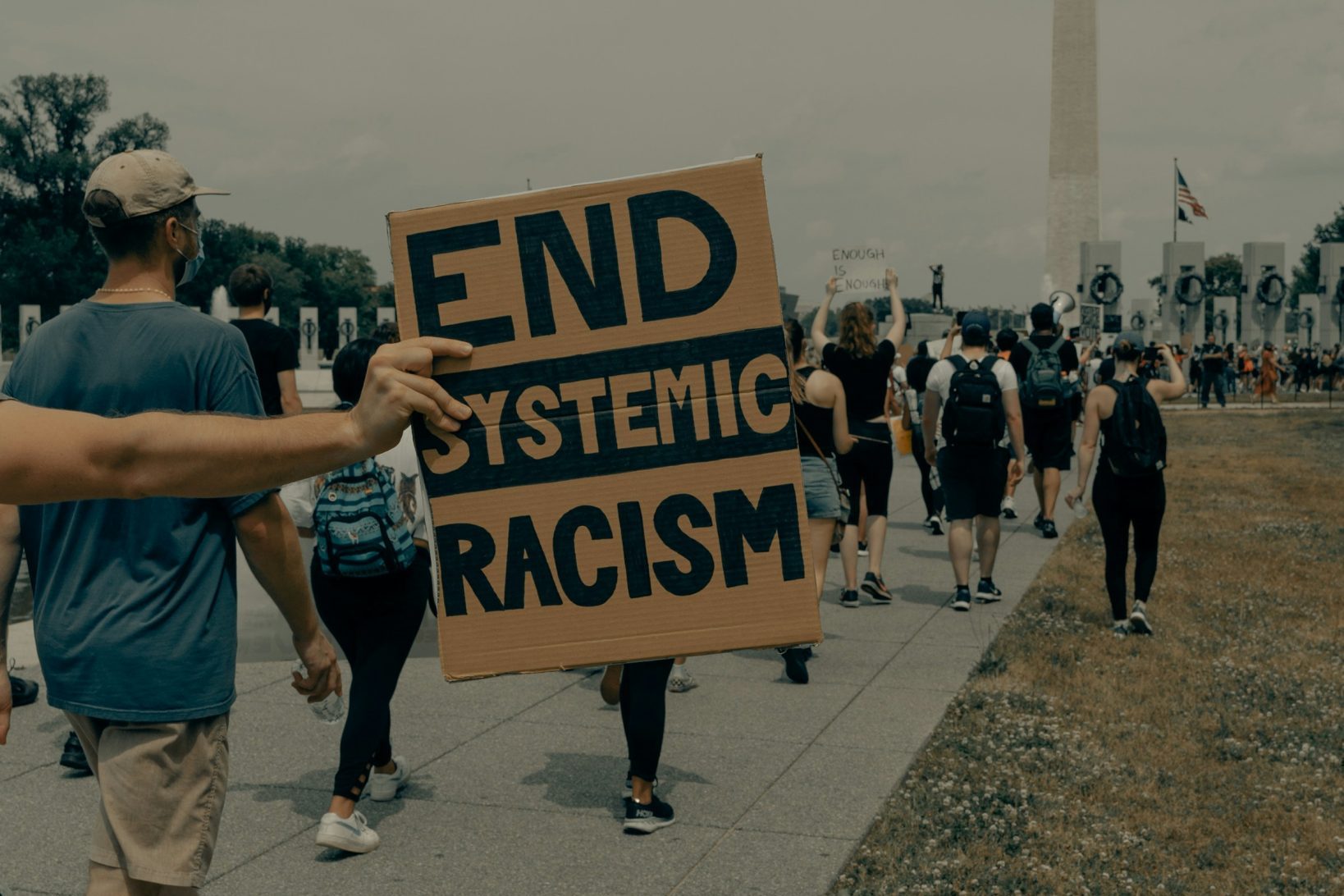 man in gray t-shirt holding black and white sign saying 'end systemic racism' Just Access mental health